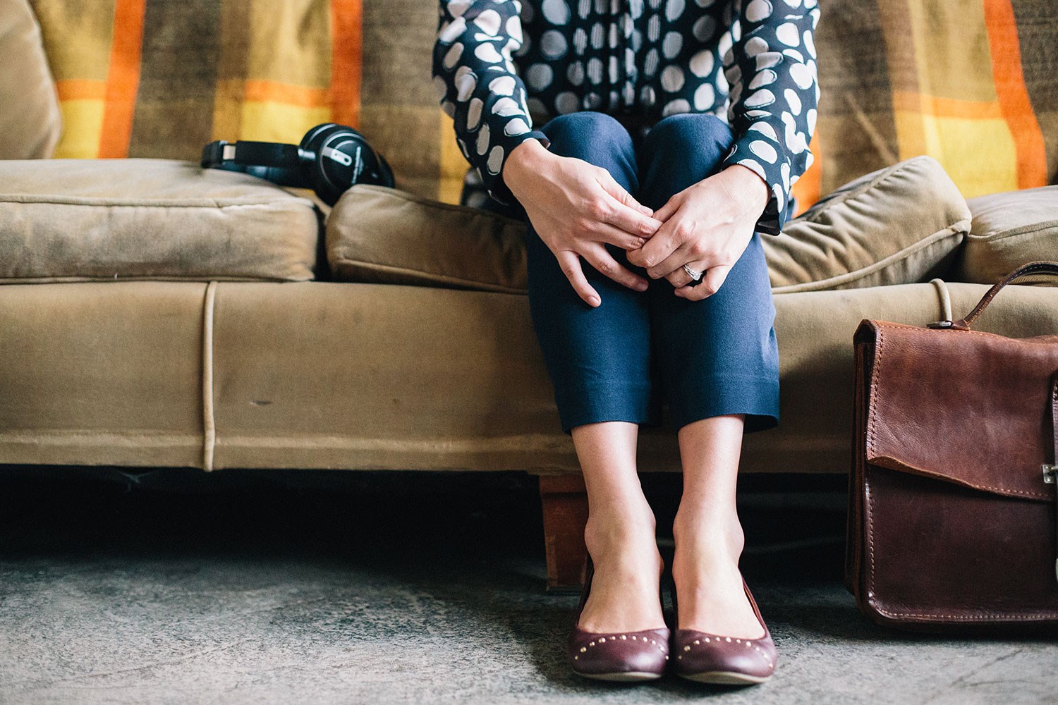 Image of woman sitting on a couch with hands crossed over knees.